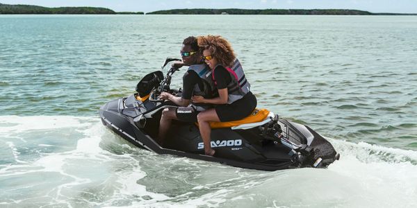 Two people riding a Sea-Doo jet ski on calm water.