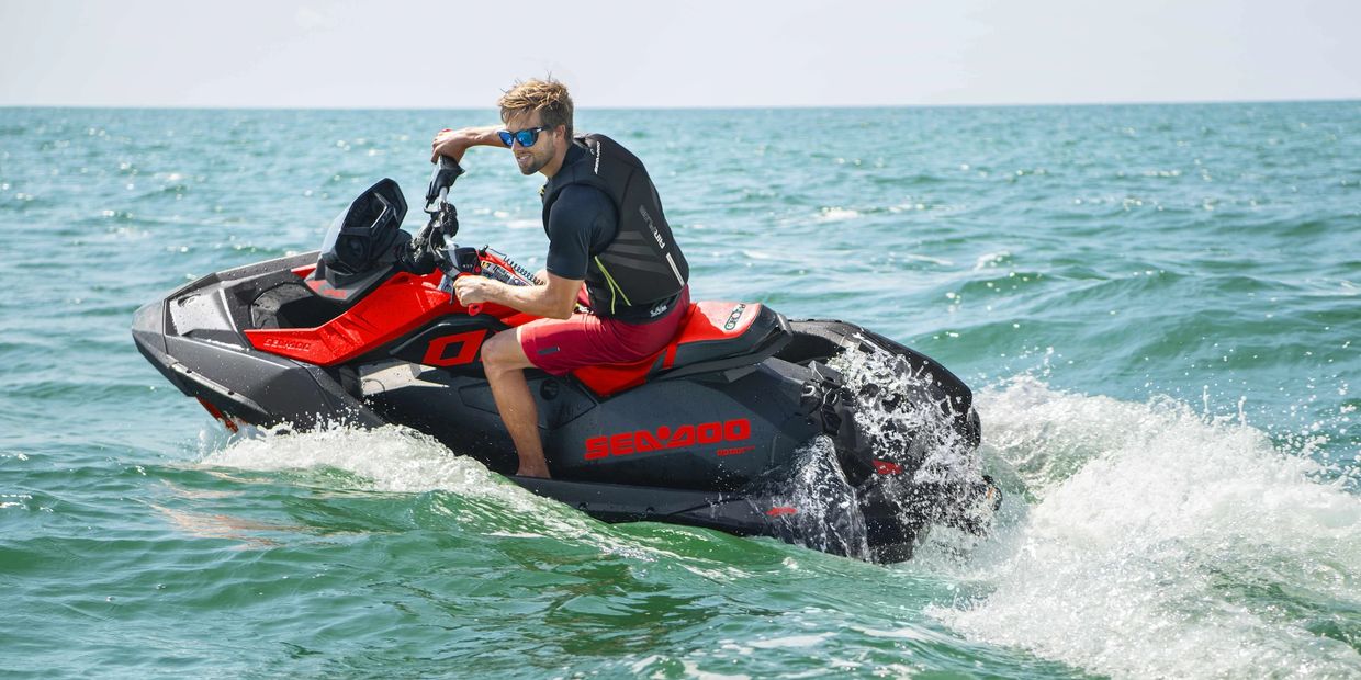 Man riding a red and black Sea-Doo jet ski on the ocean.