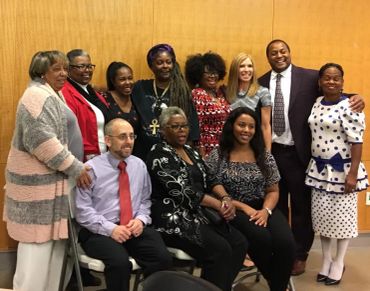 A diverse group of people posing together indoors, smiling warmly.