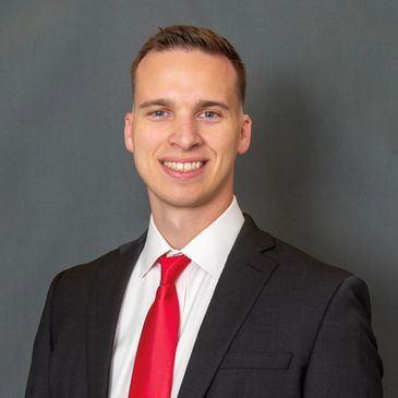 Young man in suit with red tie smiling.