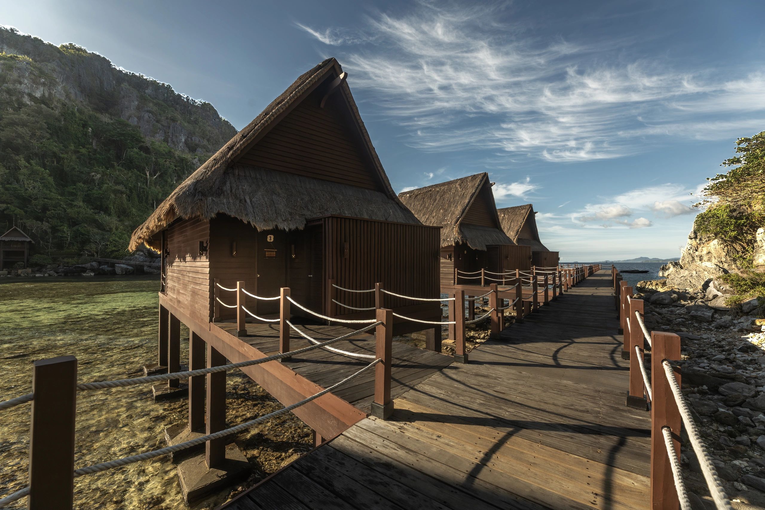 Wooden huts on stilts over clear water with mountain backdrop.