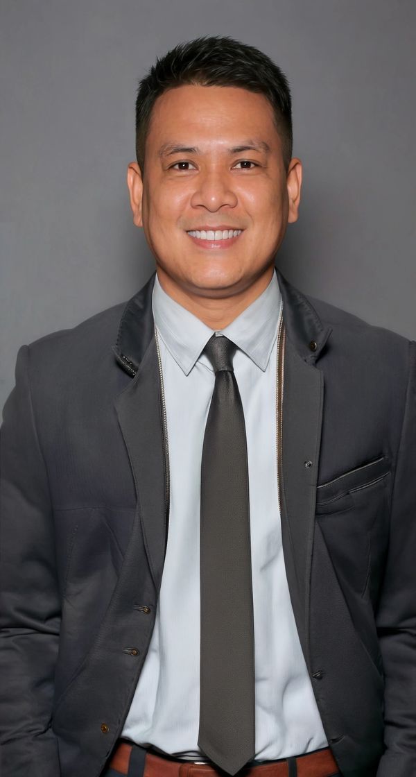 Smiling man in a dark suit and tie against a gray background.