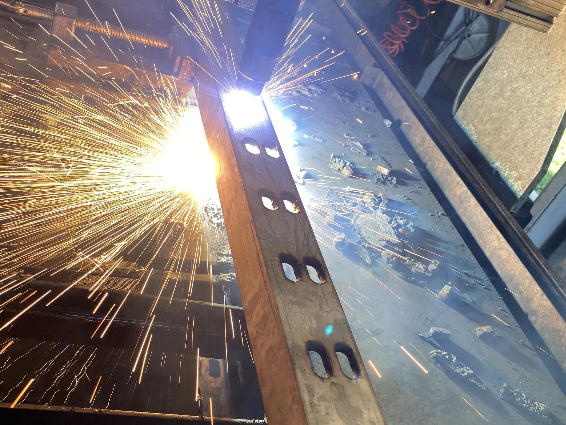 Sparks fly as metal is cut with a plasma cutter in a workshop.