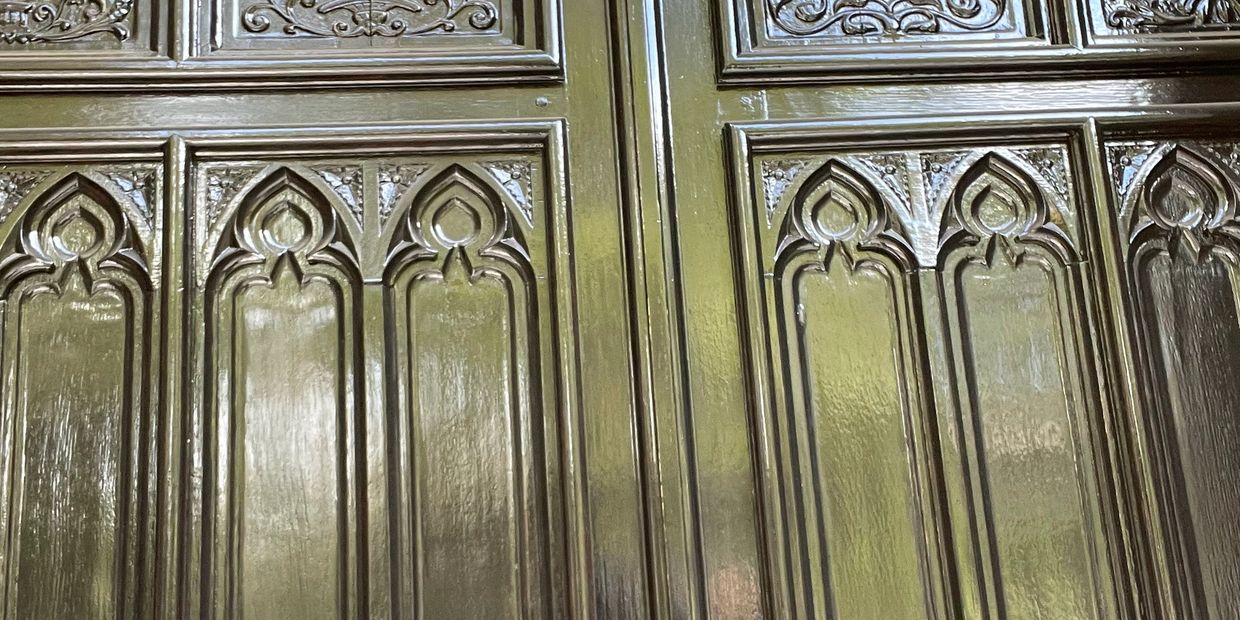 Close-up of ornate wooden door panels with carved gothic-style arch designs.