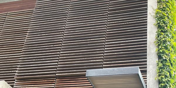 Close-up of modern wooden slats on a building exterior with some greenery on the side.