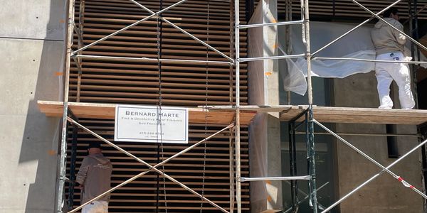 Workers on scaffolding renovating a building's exterior with wooden slats.