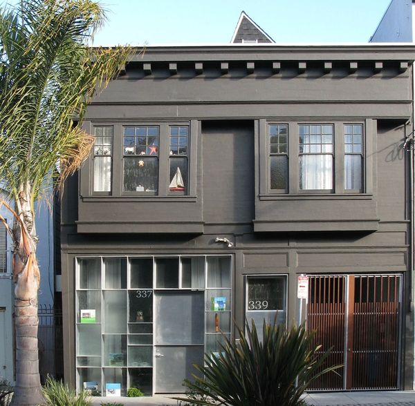 Modern gray building with large windows and plants outside.
