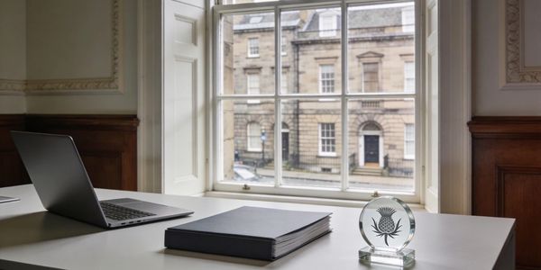 A quiet office desk with a laptop, a binder, and a glass award by a window.