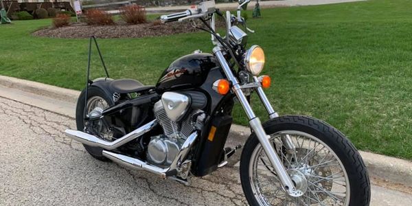 A sleek black motorcycle parked on a street near a grassy area.
