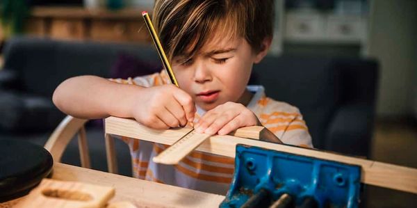 Young boy measuring and marking wood with a ruler and pencil.