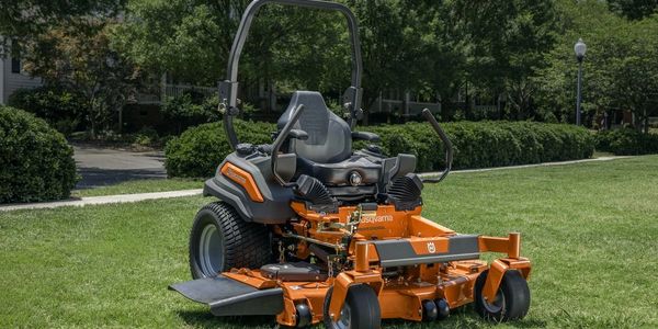 A bright orange Husqvarna zero-turn lawn mower on green grass.
