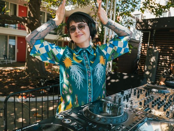 Smiling DJ wearing headphones and colorful shirt playing music outdoors.