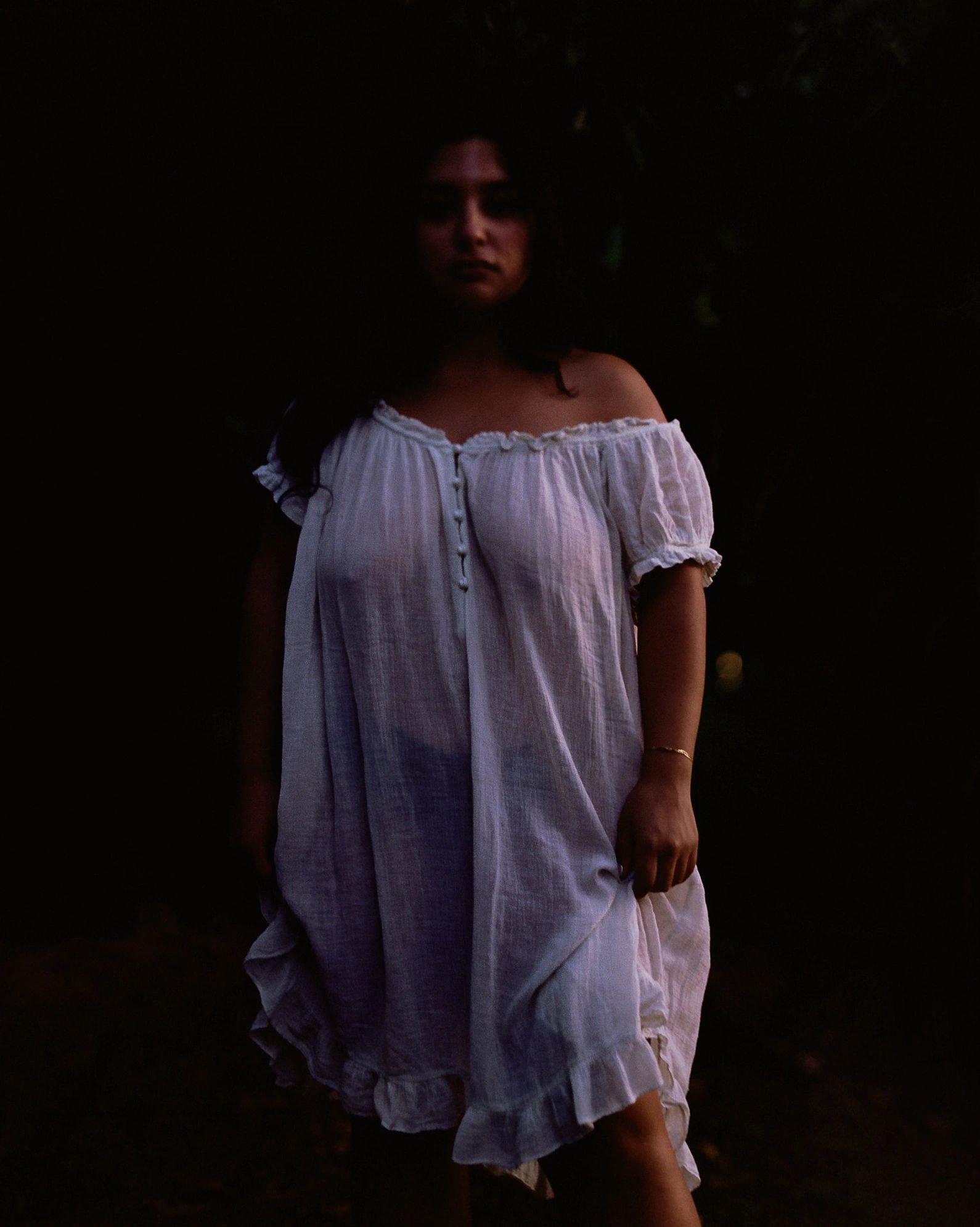 Woman in a white off-shoulder dress standing in dim light.