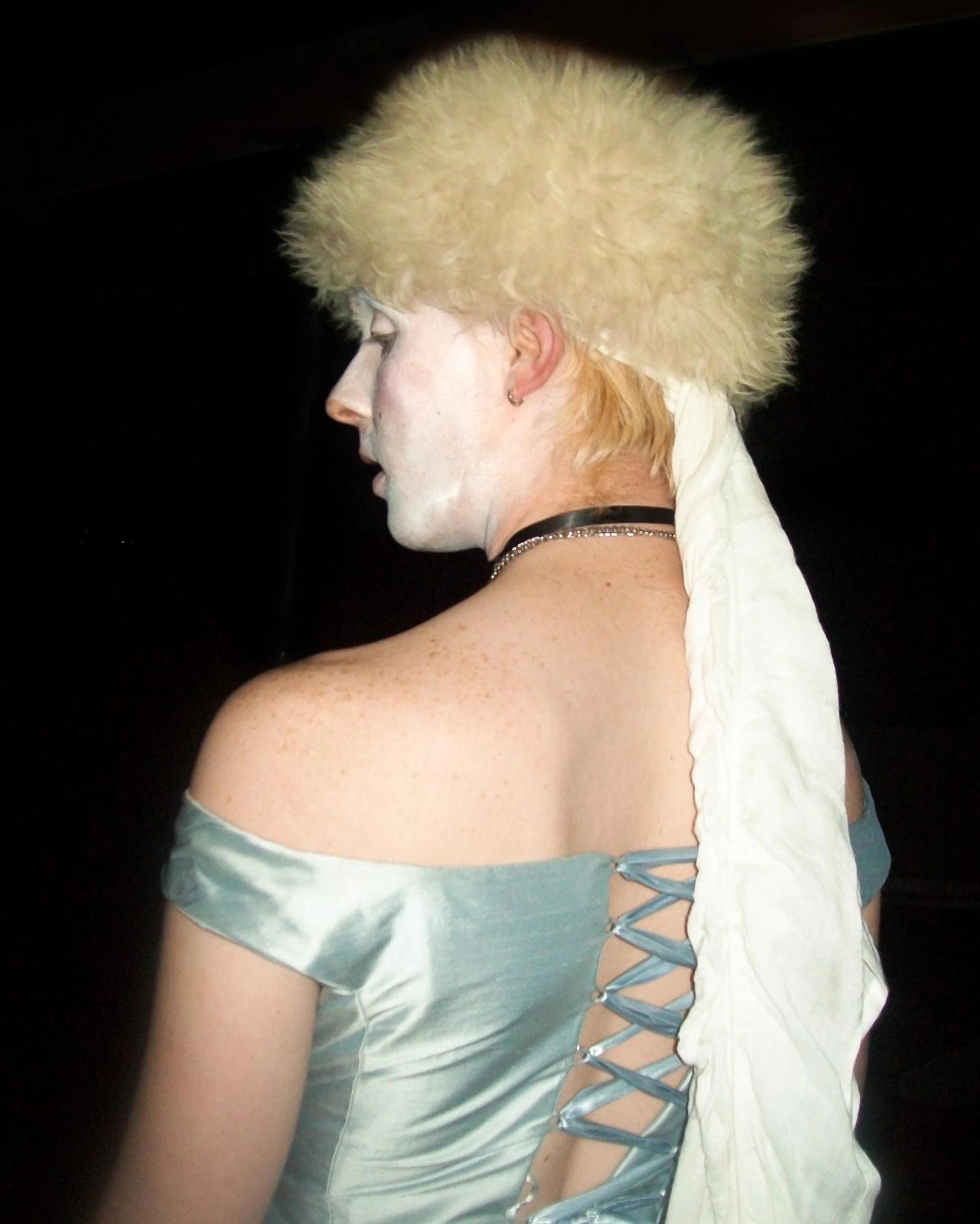 Person in vintage dress with white face paint and fluffy hat.