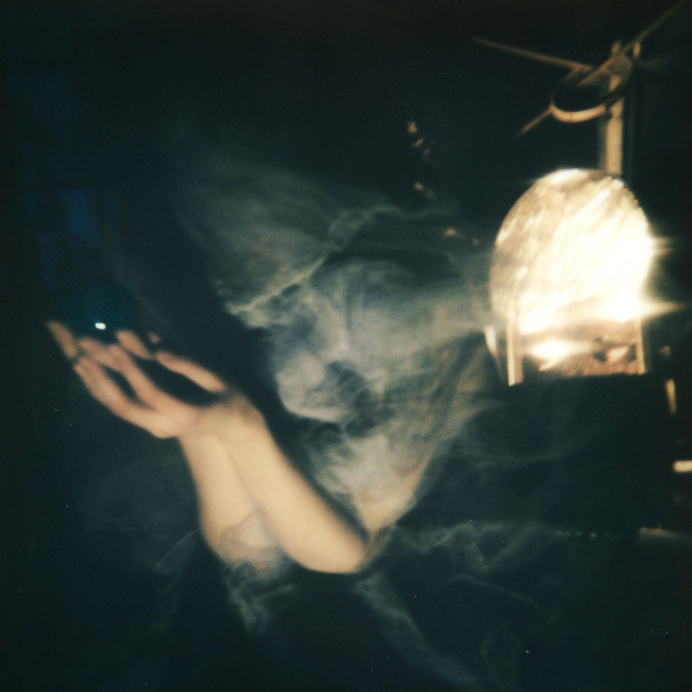 A hand reaching out into the dark with smoke and a glowing light nearby.