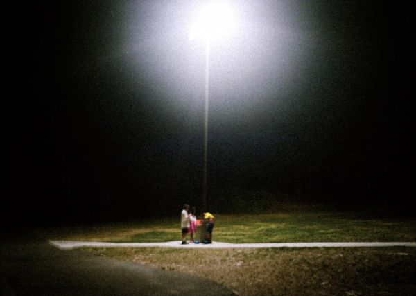 Three children standing under a bright streetlight at night.