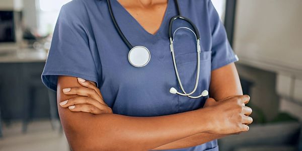 Medical professional in blue scrubs with a stethoscope crosses arms.