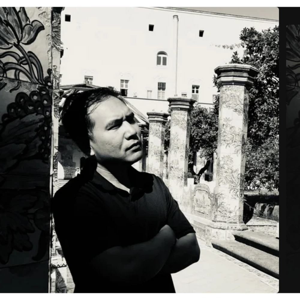 Man posing confidently against a backdrop of ornate pillars and building.