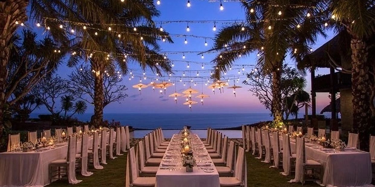 Elegant outdoor dining setup at sunset with string lights and ocean view.