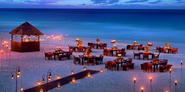 Romantic candlelit dinner setup on a beach at twilight.