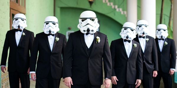 Group of men in tuxedos wearing stormtrooper helmets.