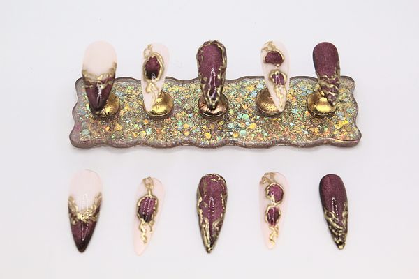 Decorative set of artificial nails with gold and purple designs on a glittery base.