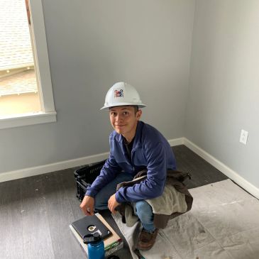 Young man in construction gear crouches indoors.