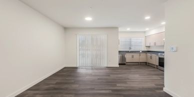 Empty modern kitchen and living area with gray wooden floor.