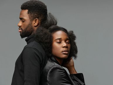 A serene couple stands back to back with closed eyes against a gray background.