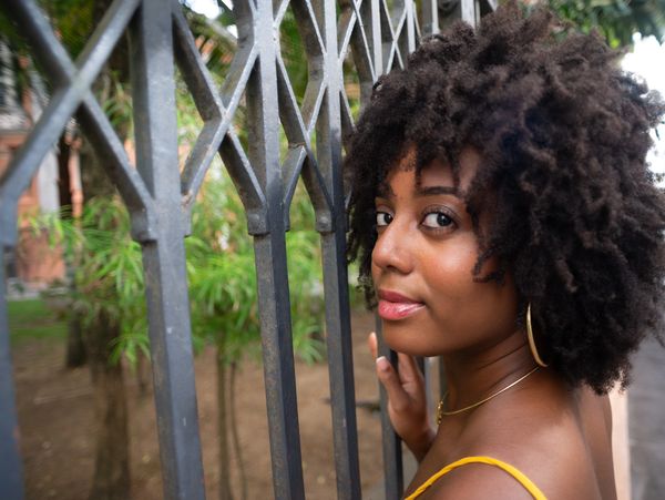 Young woman with curly hair by an iron fence, looking back.