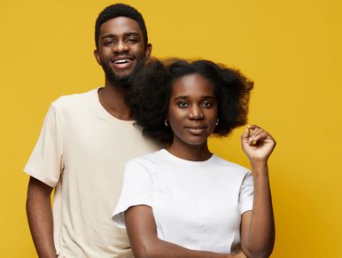 A smiling man and a confident woman posing against a yellow background.