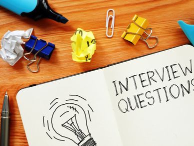 Notebook open to interview questions with office supplies on wooden desk.