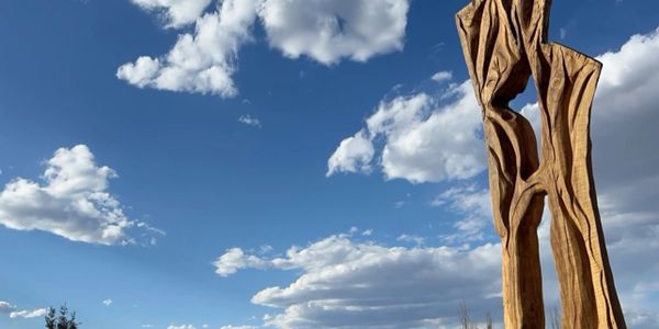 Tall wooden sculpture against a bright blue sky with clouds.