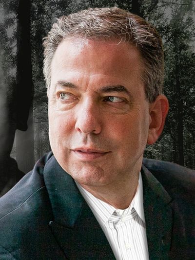 Man in a suit looking to the side with forest background.