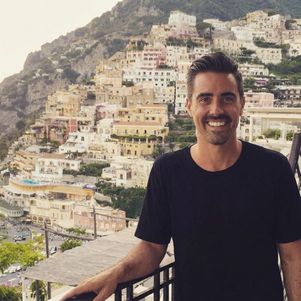 Man smiling in front of a hillside town.