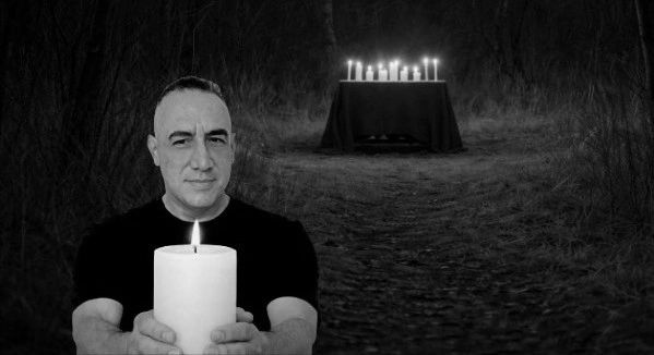 James holding a lit white candle in front of a mystical altar setting.
