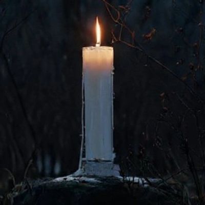 Lit white candle burning in dark setting for New Moon spell ritual.