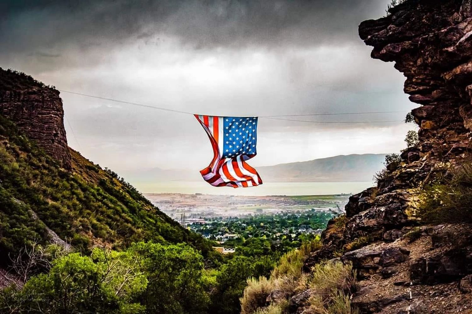 American flag hanging between two cliffs over a scenic valley. Grove Canyon located in Pleasant Grove, Utah.
