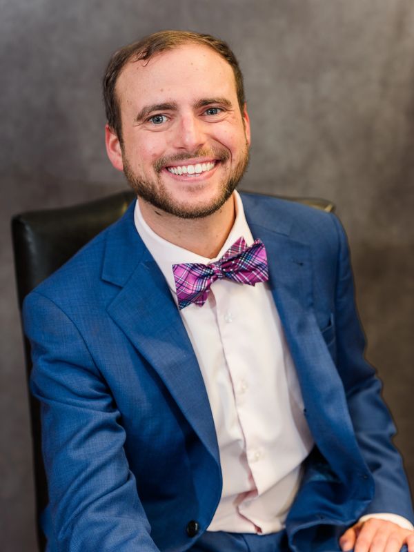 Man in blue suit with pink bow tie smiling.