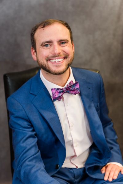 Man in a blue suit and plaid bow tie smiling.