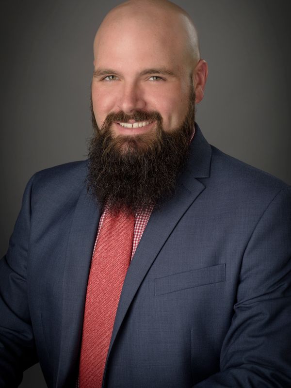 Smiling bald man with a thick beard in a suit and red tie.