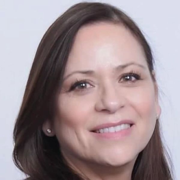 Close-up of a smiling woman with brown hair against a light background.