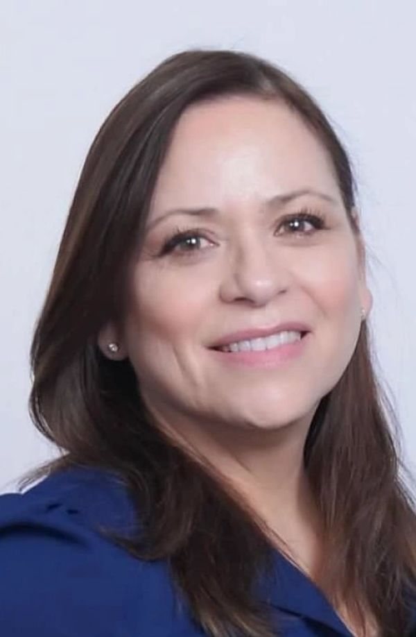 Close-up of a smiling woman with brown hair against a light background.