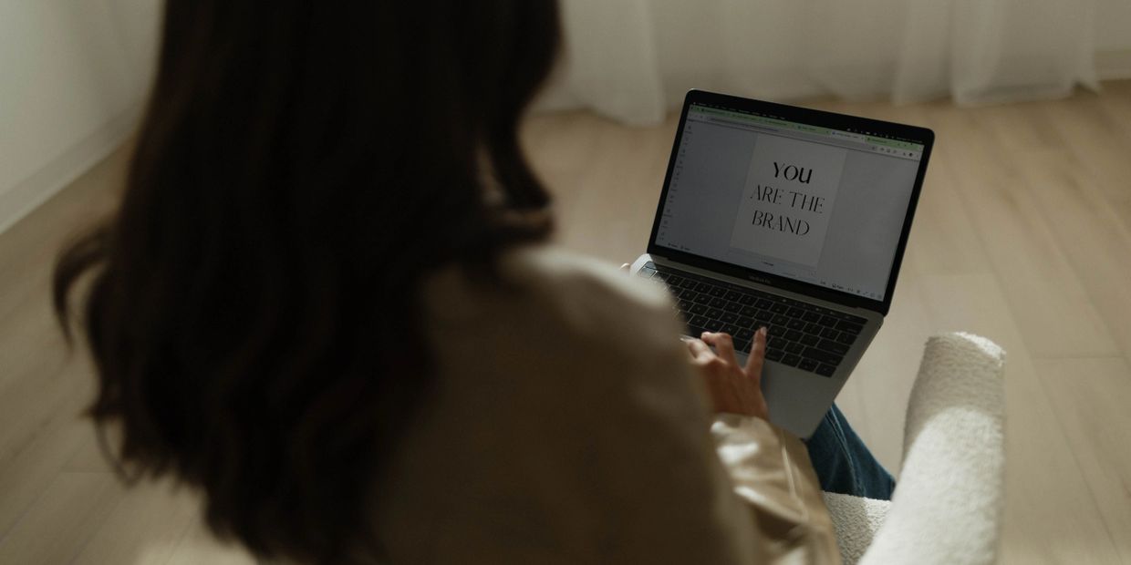 Person working on a laptop with "YOU ARE THE BRAND" on screen.
