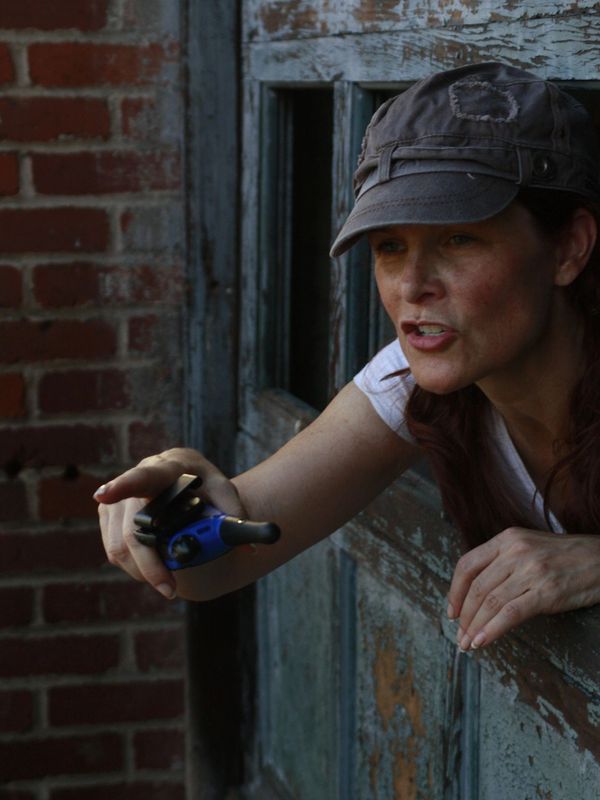 Anne Welles directing on set, pointing a camera through a rustic window