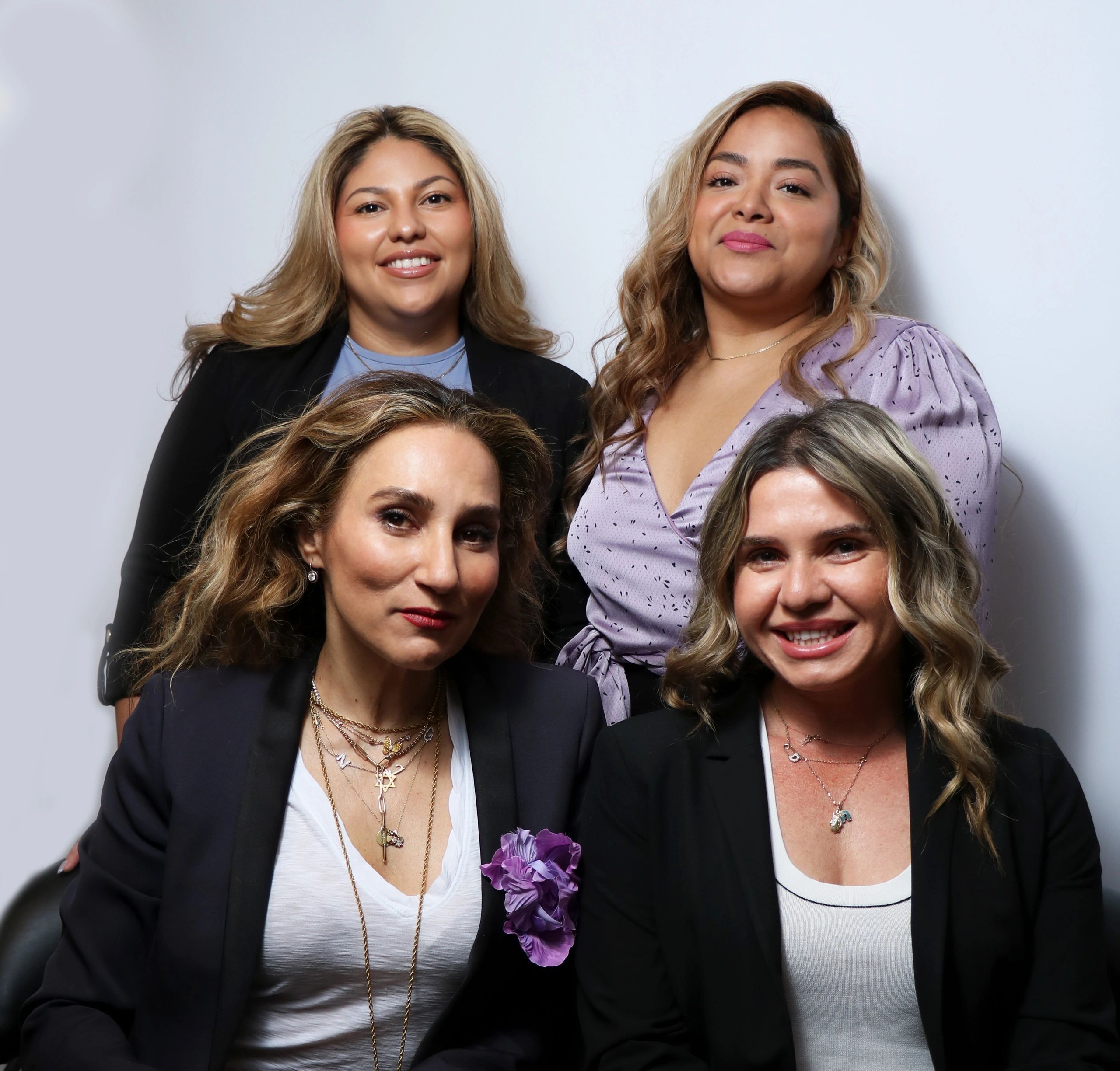 Four women posing confidently in smart casual attire against a plain backdrop.