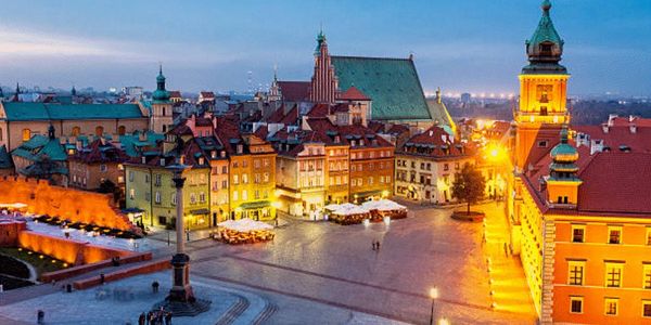 Evening view of a historic European town square with colorful buildings and warm street lighting.
