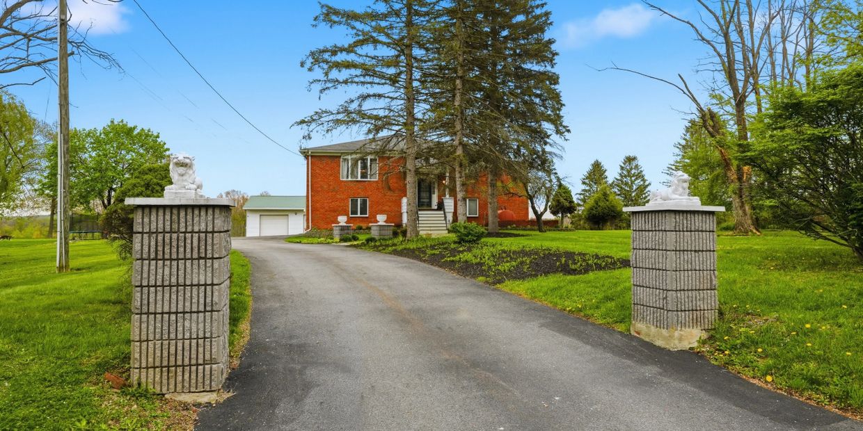 Brick house with a long driveway and stone pillars topped with lion statues.