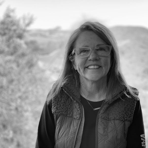 Smiling woman wearing glasses and a vest in an outdoor setting.