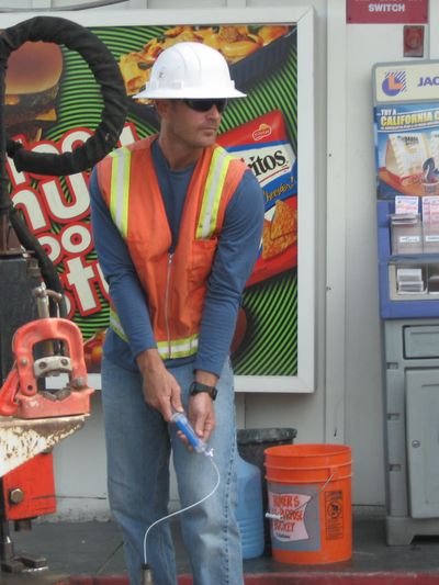 Construction worker in safety gear using equipment at a site with snack advertisement background.